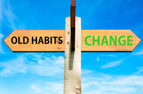 photo of a wooden signpost with two arrows pointing in opposite directions saying old habits and change, with clear blue sky behind